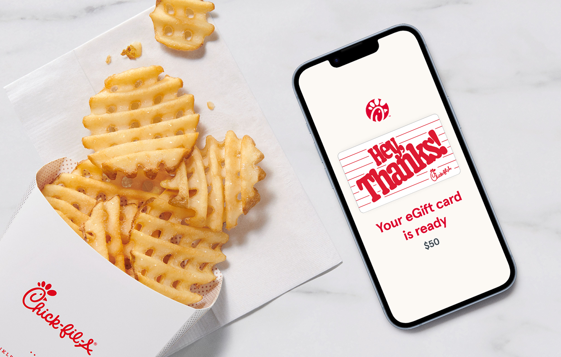 A smartphone with a Chick-fil-A® eGift card on the screen that says “Hey, Thanks!”, sitting next to Waffle Fries