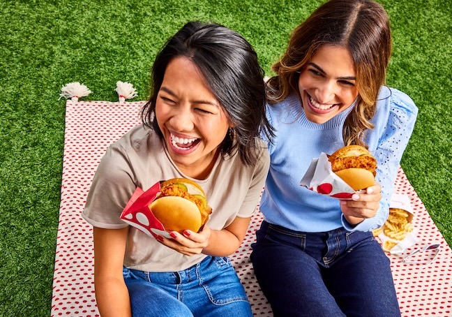 Two people sitting together outside on a blanket, each holding a Chick-fil-A® Chicken Sandwich